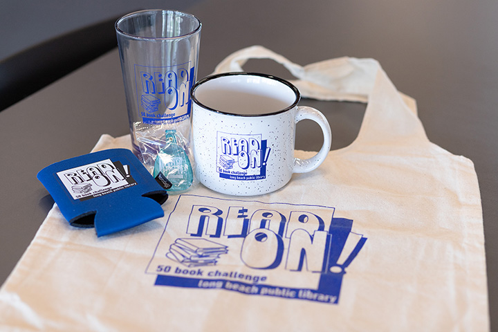 Photo of the 2025 50 Book Challenge prizes (left to right): A koozie, keychain, glass cup, mug, and tote that say "Read on!"